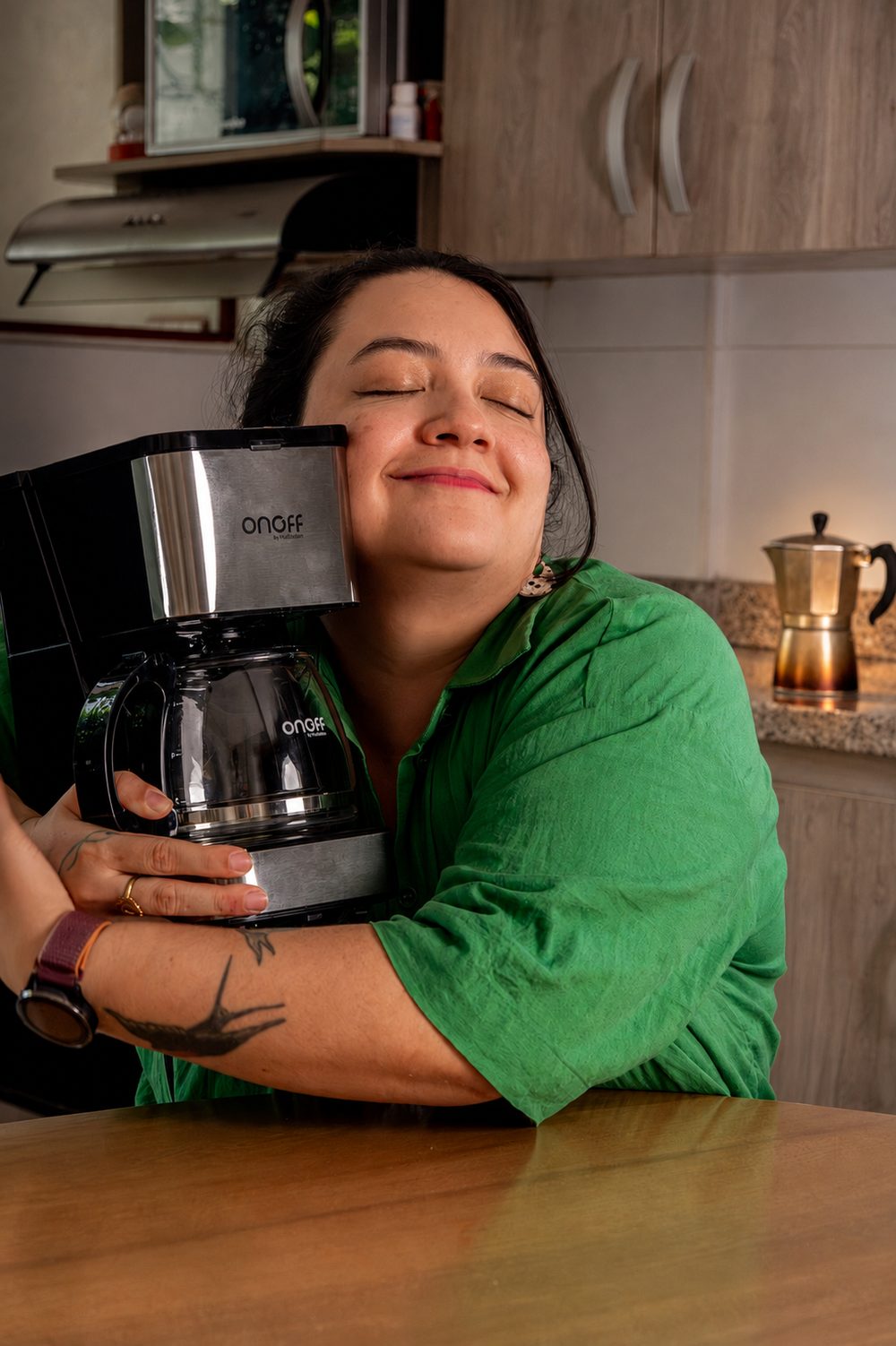 A woman in a green shirt hugging an Onoff coffee maker, eyes closed